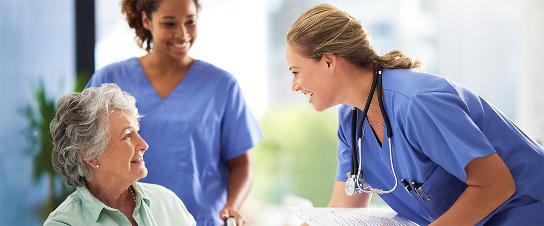 Two female nurses smiling leaning down to welcome a new patient