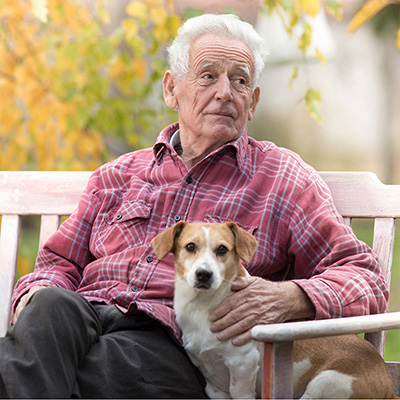 elderly man sitting outside on a bench with a dog